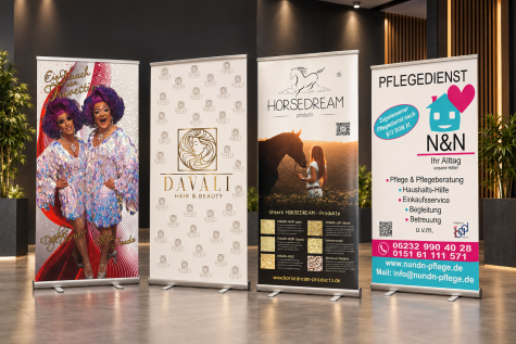 Vier aufgestellte Roll-up-Banner in einem modernen Innenraum mit unterschiedlichen Werbemotiven.