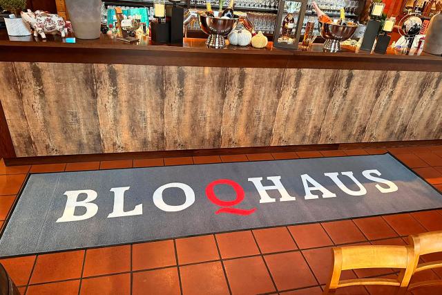Restaurantbar mit rustikalem Tresen und einer Bodenmatte mit dem Schriftzug BLOQHAUS.
