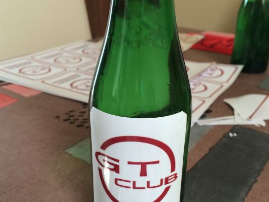 Grüne Sektflasche mit roter Kapsel und weißem Etikett auf einem Tisch