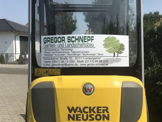 Rückseite eines gelben Wacker Neuson Baggers mit Firmenwerbung auf der Heckscheibe