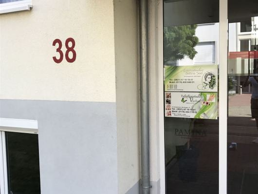 Eingang eines Gebäudes mit der Hausnummer 38 und einer Glastür mit Werbeplakat.