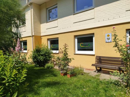 Sonniger Garten vor einem gelb gestrichenen Haus mit Bank und Blumen.