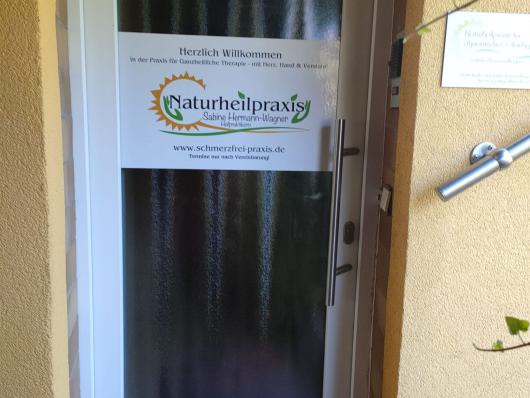 Eingangstür einer Naturheilpraxis mit Schild an der Glastür