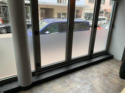 Blick aus einem leeren Raum durch große Fenster auf parkende Autos an einer Straße