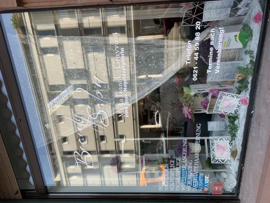 Schaufenster eines Beauty-Studios mit Blumen, Bilderrahmen und Schriftzügen auf der Scheibe.
