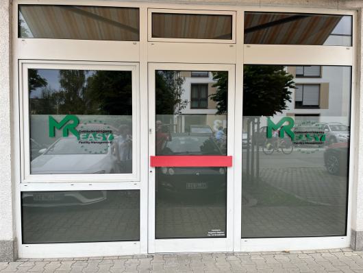 Gläserne Eingangstür eines Geschäfts mit MR Gebäudereinigung und rotem Türgriff