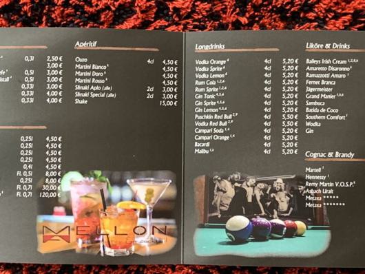 Aufgeklappte Getränkekarte mit zahlreichen Cocktail-, Kaffee- und Whisky-Angeboten auf dunklem Hintergrund.