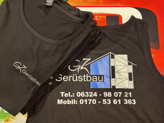 Mehrere schwarze Tanktops mit Gerüstbau-Aufdruck liegen auf einer farbigen Oberfläche.