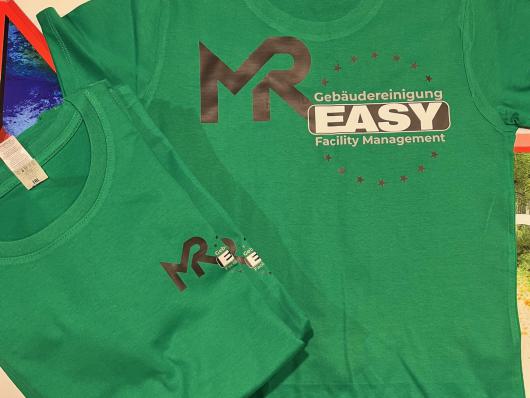 Zwei grüne T-Shirts mit aufgedrucktem Firmenlogo liegen übereinander auf einem Tisch.