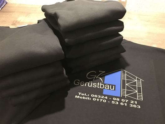 Mehrere gefaltete schwarze Textilien mit aufgedrucktem Firmenlogo liegen übereinander.