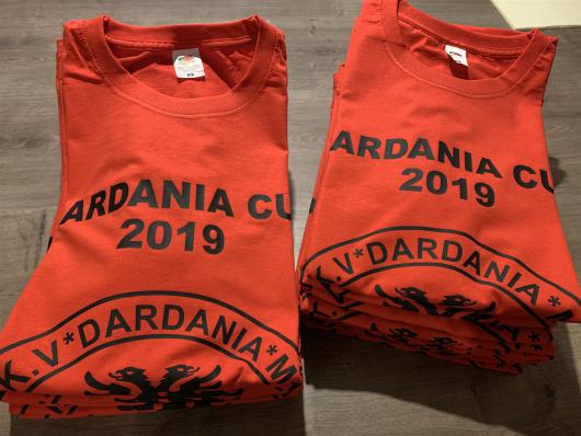 Zwei gefaltete rote T-Shirts mit schwarzem Aufdruck liegen auf einem Holzboden.