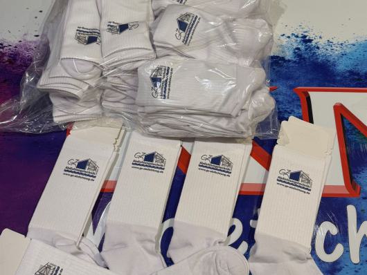 Mehrere weiße Socken mit Logo, teils lose und teils in Plastik verpackt auf einem Tisch.