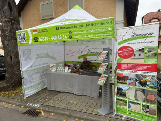 Messestand unter einem grünen Werbezelt für einen Steinreinigungsbetrieb auf einem Gehweg.