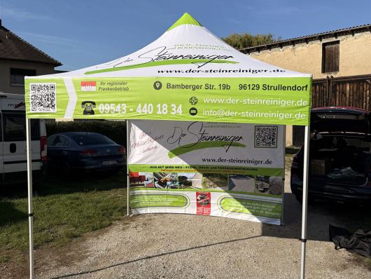 Werbezelt mit Banner für einen Steinreinigungsdienst auf einem Parkplatz vor Gebäuden.