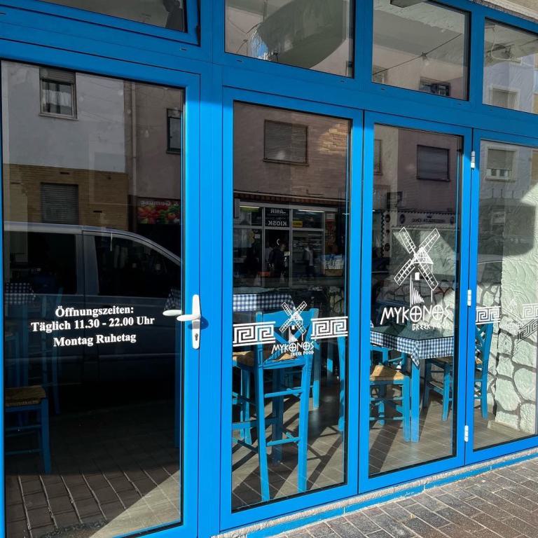 Blaue verglaste Eingangstür eines Restaurants mit Öffnungszeiten und Blick auf Tische im Innenraum.