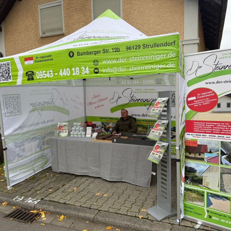 Messestand eines Reinigungsunternehmens mit grün-weißem Pavillon, Tisch und Werbebanner an einer Straße.
