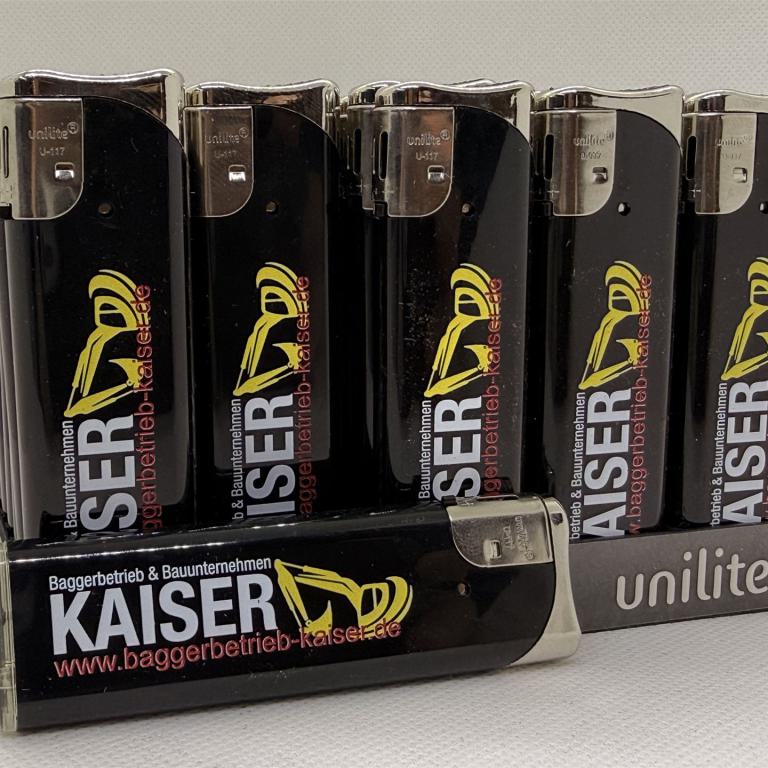 Mehrere schwarze Feuerzeuge mit Kaiser Aufdruck in einem Unilite Aufsteller.