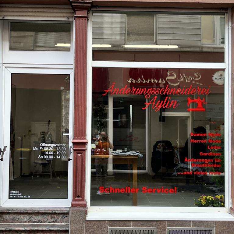 Schaufenster und Eingang einer Änderungsschneiderei mit roter Beschriftung an der Glasscheibe.