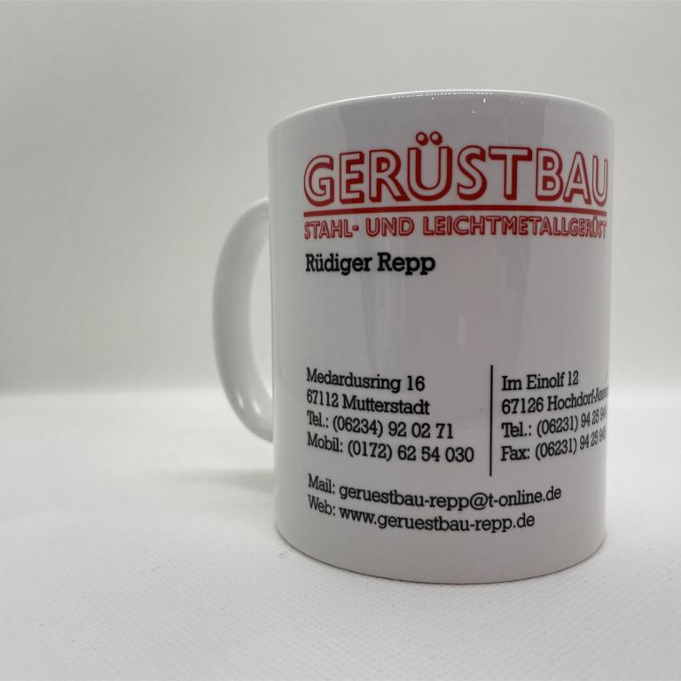 Weiße Keramiktasse mit rotem und schwarzem Firmenaufdruck für Gerüstbau auf weißem Hintergrund.