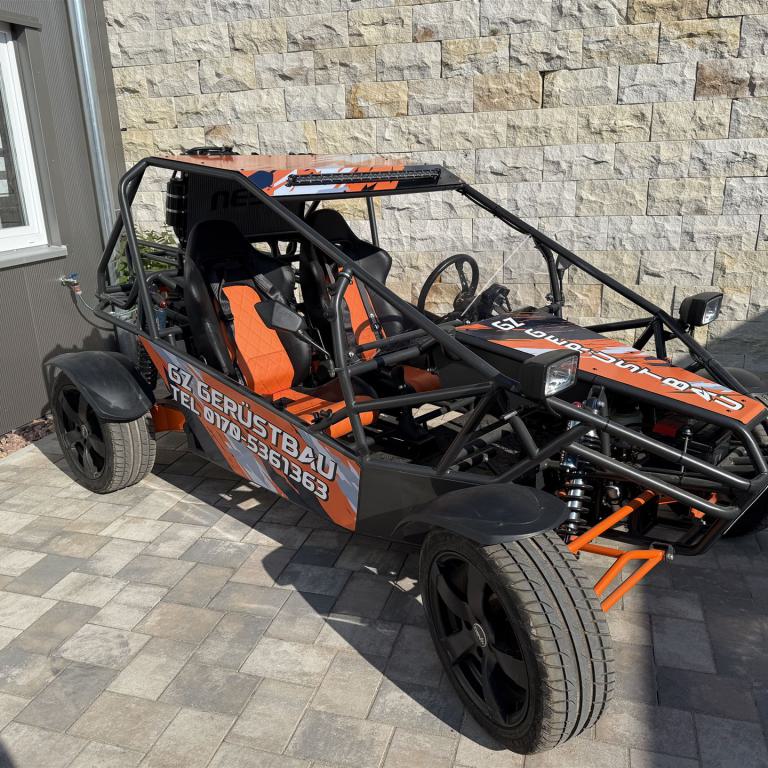 Offenes schwarzes und oranges Buggy-Fahrzeug mit Überrollkäfig auf gepflasterter Einfahrt