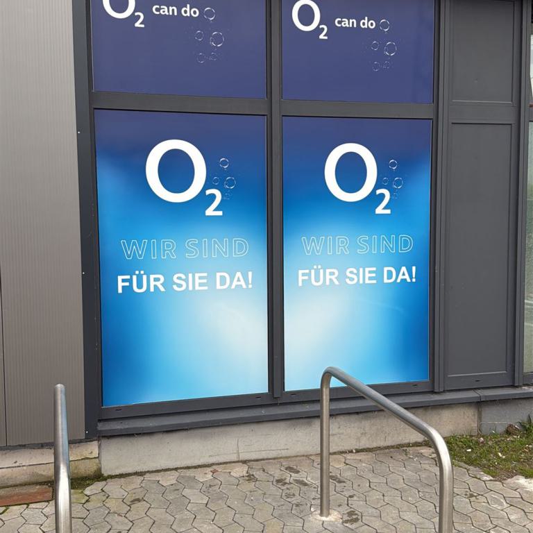 Schaufenster eines O2-Geschäfts mit blauen Werbeflächen und Fahrradständern davor.