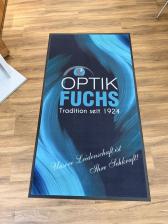 Große blaue Bodenmatte von Optik Fuchs auf einem Holzfußboden