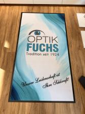 Große Bodenmatte mit dem Schriftzug OPTIK FUCHS auf Holzfußboden